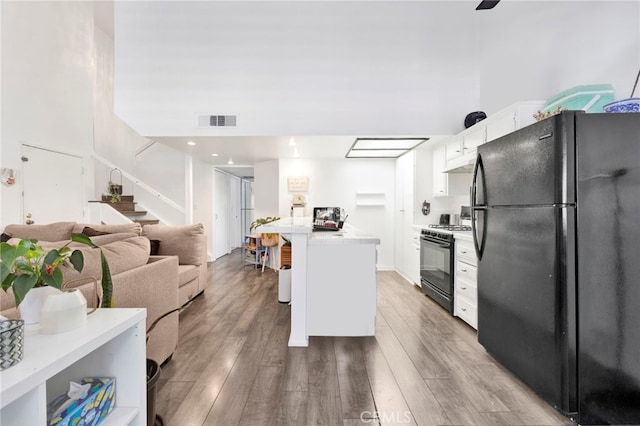 kitchen featuring black refrigerator, hardwood / wood-style floors, white cabinetry, a high ceiling, and gas range oven