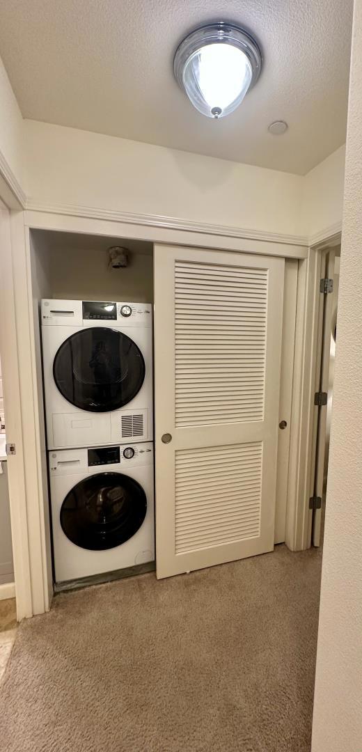 washroom featuring stacked washer / drying machine, carpet flooring, and a textured ceiling