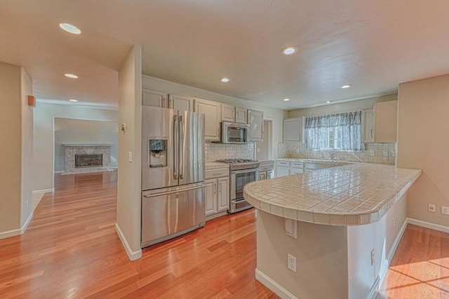 kitchen with tile countertops, a breakfast bar area, kitchen peninsula, stainless steel appliances, and light wood-type flooring