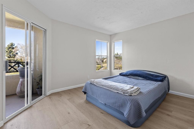 bedroom with multiple windows, access to exterior, light hardwood / wood-style flooring, and a textured ceiling