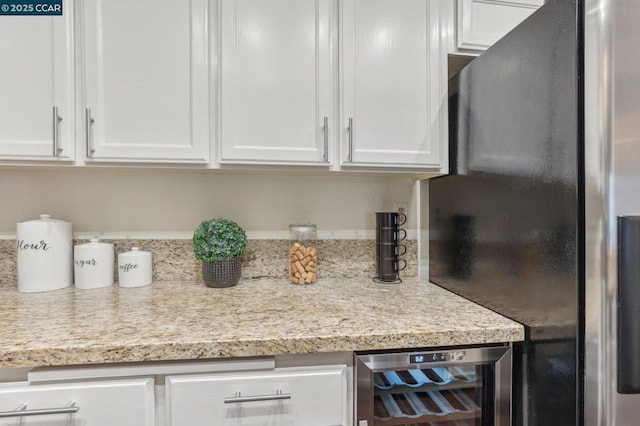 kitchen featuring wine cooler, light stone counters, white cabinetry, and stainless steel refrigerator