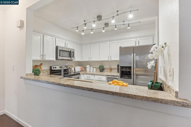 kitchen with stainless steel appliances, light stone countertops, kitchen peninsula, and white cabinets