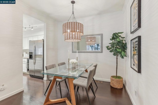 dining room with crown molding, rail lighting, dark wood-type flooring, and an inviting chandelier