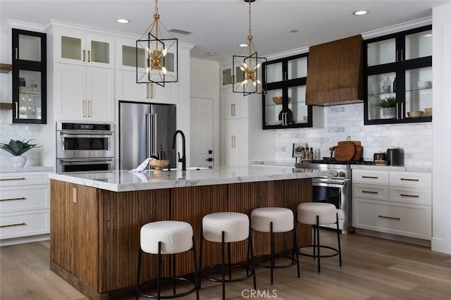 kitchen featuring decorative light fixtures, a large island with sink, premium range hood, sink, and high quality appliances