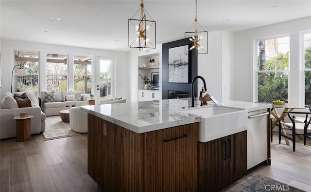 kitchen featuring a center island with sink, sink, wood-type flooring, stainless steel dishwasher, and hanging light fixtures