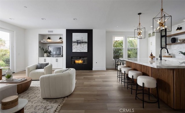 bar featuring light wood-type flooring, sink, and a large fireplace