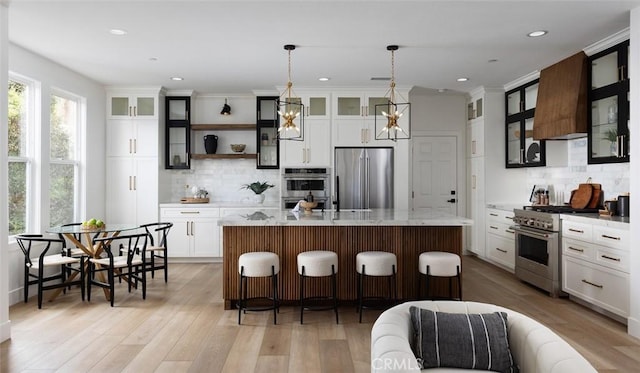 kitchen with a center island with sink, light hardwood / wood-style flooring, decorative light fixtures, high quality appliances, and a kitchen breakfast bar