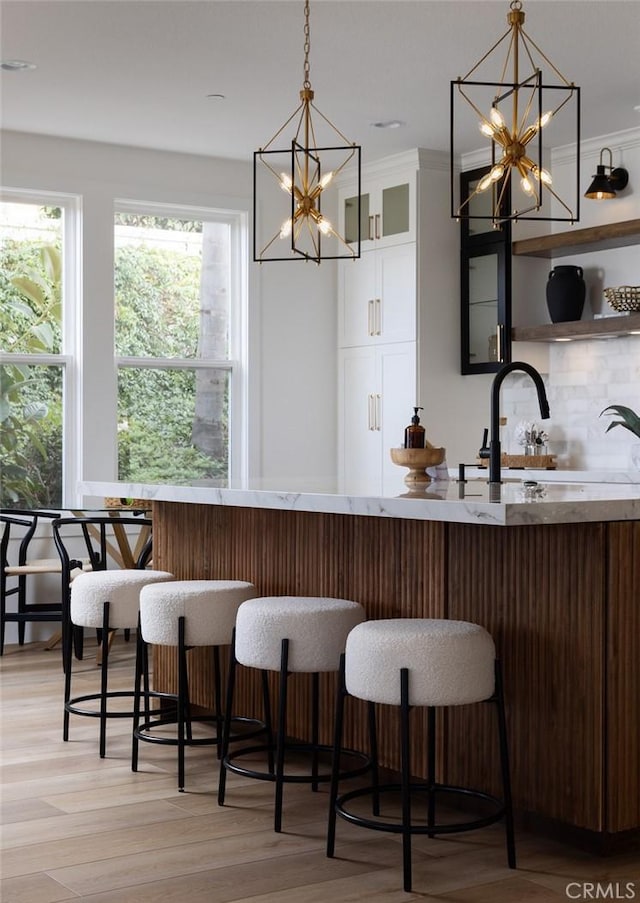 kitchen featuring backsplash, hanging light fixtures, light hardwood / wood-style floors, and bar