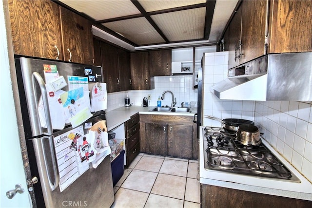 kitchen featuring sink, light tile patterned floors, stainless steel refrigerator, dark brown cabinetry, and white gas cooktop