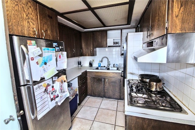 kitchen with light tile patterned floors, gas cooktop, dark brown cabinetry, a sink, and freestanding refrigerator