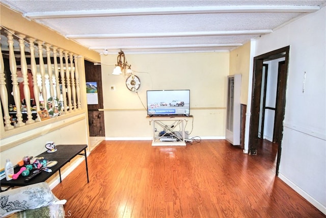 interior space featuring a textured ceiling, baseboards, beamed ceiling, and wood finished floors