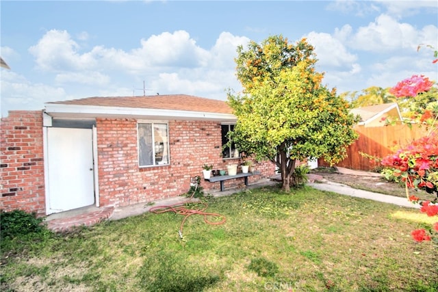 rear view of property featuring fence, a lawn, and brick siding