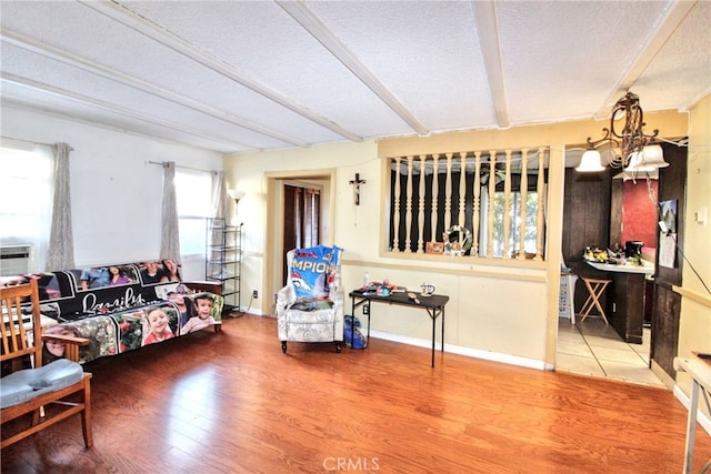 sitting room with a textured ceiling, a chandelier, wood finished floors, baseboards, and beamed ceiling