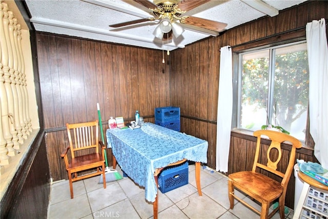 interior space featuring ceiling fan, wooden walls, a textured ceiling, and light tile patterned flooring