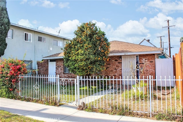 view of front of home featuring a fenced front yard, roof with shingles, and brick siding