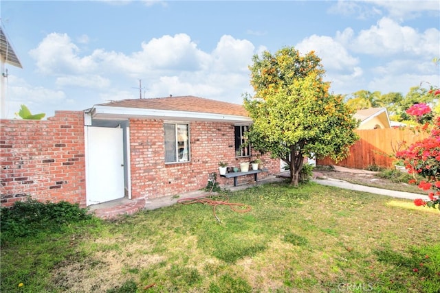 rear view of property featuring a yard, brick siding, and fence