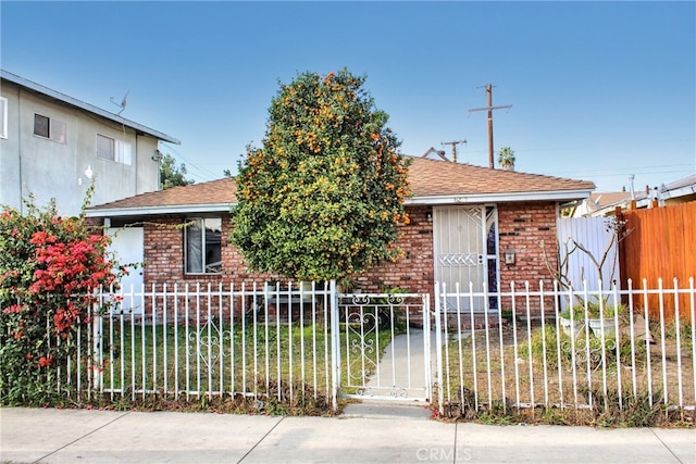 bungalow-style house featuring a fenced front yard, roof with shingles, and brick siding