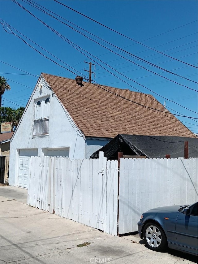 exterior space featuring a garage, roof with shingles, fence, an outdoor structure, and stucco siding