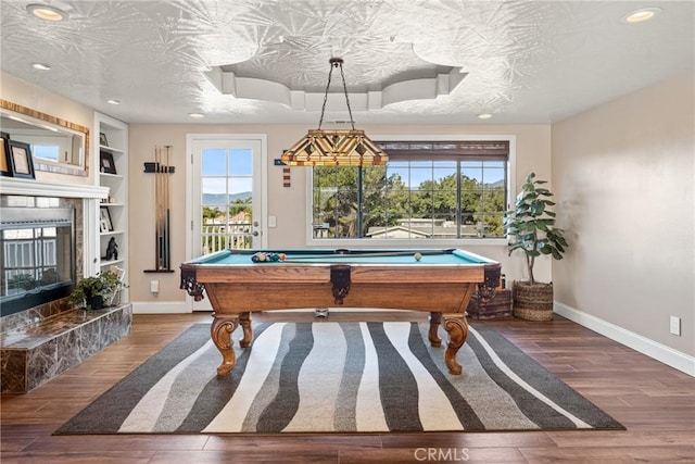 playroom with a tile fireplace, billiards, hardwood / wood-style flooring, a textured ceiling, and built in shelves