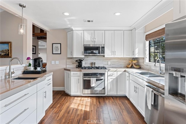 kitchen with white cabinetry, stainless steel appliances, decorative light fixtures, and sink