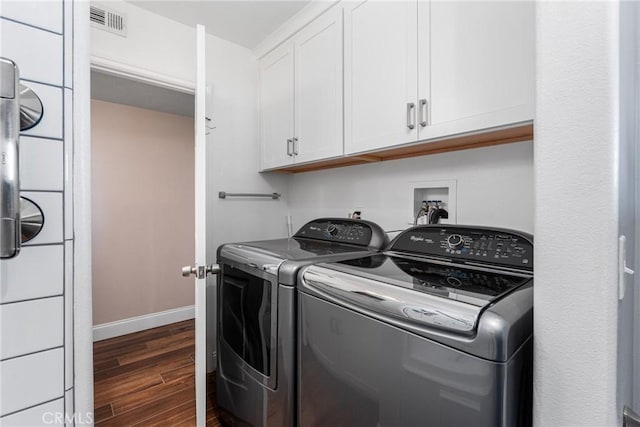 clothes washing area with dark wood-type flooring, cabinets, and washer and dryer