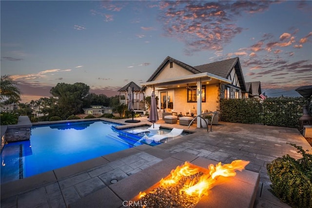 pool at dusk with an outdoor living space with a fire pit, a patio, and an in ground hot tub