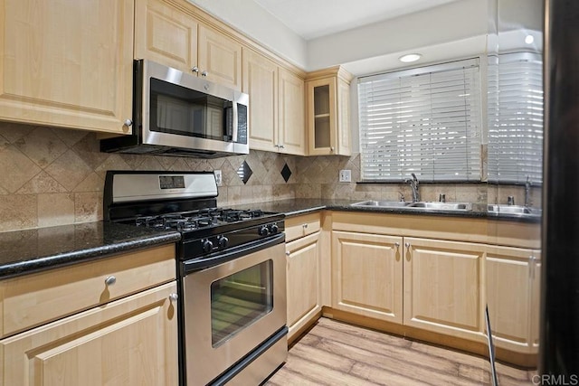 kitchen featuring appliances with stainless steel finishes, tasteful backsplash, sink, dark stone counters, and light hardwood / wood-style flooring