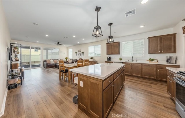 kitchen featuring hanging light fixtures, light hardwood / wood-style flooring, stainless steel range with gas stovetop, a kitchen island, and a healthy amount of sunlight