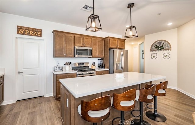 kitchen featuring appliances with stainless steel finishes, a center island, light wood-type flooring, and decorative light fixtures