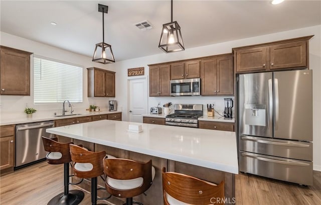 kitchen with a breakfast bar area, hanging light fixtures, stainless steel appliances, light hardwood / wood-style floors, and a kitchen island