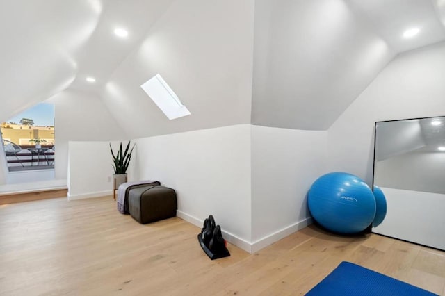 exercise room featuring lofted ceiling with skylight and light hardwood / wood-style flooring