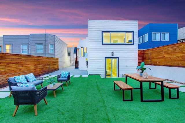 back house at dusk with an outdoor living space and a lawn