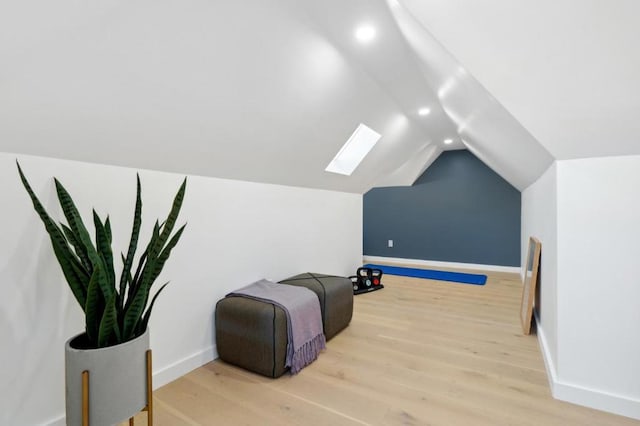 living area featuring lofted ceiling with skylight and light hardwood / wood-style flooring