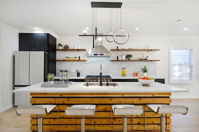 kitchen with hanging light fixtures, backsplash, light hardwood / wood-style floors, and wall chimney exhaust hood