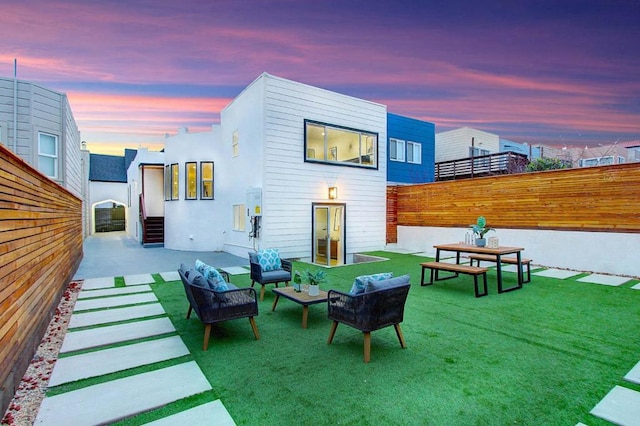 back house at dusk featuring a yard, an outdoor hangout area, and a patio area