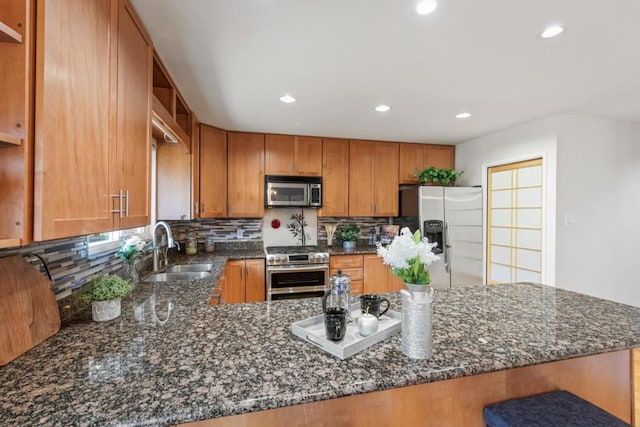 kitchen featuring appliances with stainless steel finishes, kitchen peninsula, sink, and dark stone countertops