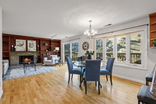 dining room featuring a notable chandelier, built in shelves, track lighting, and light hardwood / wood-style floors