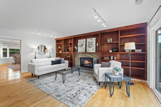 living room featuring a premium fireplace, rail lighting, light wood-type flooring, and built in shelves