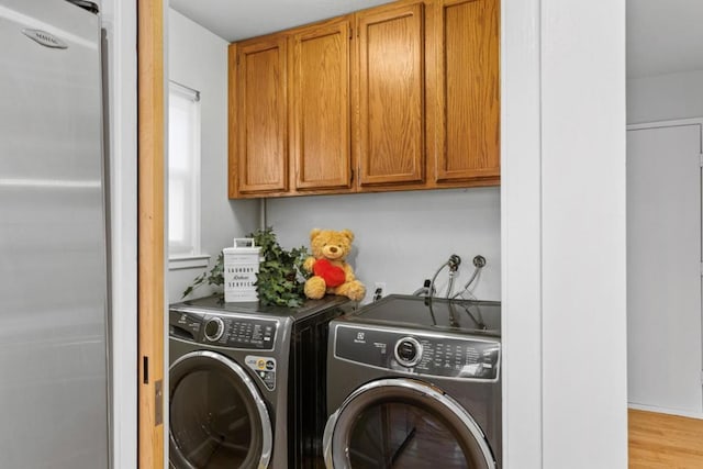 laundry room with light hardwood / wood-style floors, cabinets, and washing machine and clothes dryer