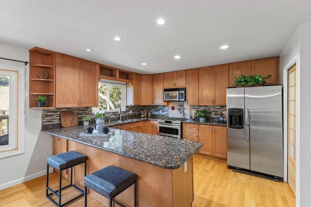 kitchen featuring stainless steel appliances, a kitchen bar, kitchen peninsula, and light wood-type flooring