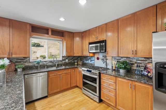 kitchen with tasteful backsplash, sink, dark stone countertops, stainless steel appliances, and light hardwood / wood-style flooring