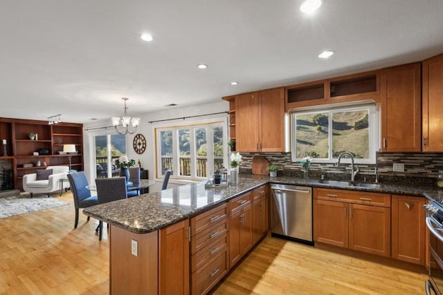 kitchen featuring appliances with stainless steel finishes, decorative light fixtures, sink, dark stone counters, and kitchen peninsula