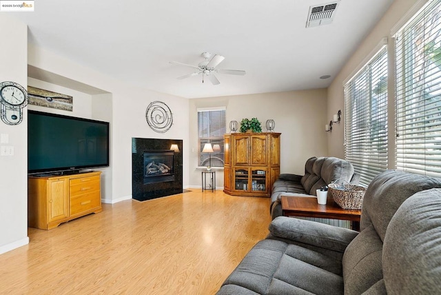 living room featuring a tile fireplace, ceiling fan, and light hardwood / wood-style floors