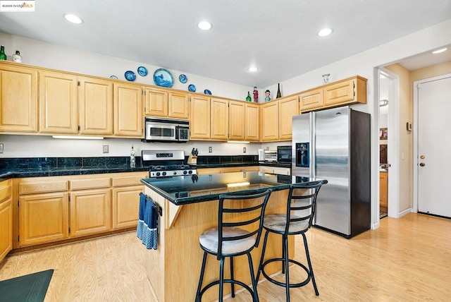 kitchen with appliances with stainless steel finishes, a breakfast bar area, light hardwood / wood-style floors, and a kitchen island