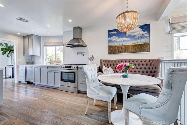 kitchen featuring stainless steel gas range, extractor fan, gray cabinetry, pendant lighting, and light hardwood / wood-style floors