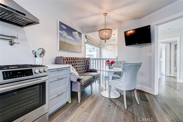 kitchen with range hood, stainless steel gas range, light hardwood / wood-style floors, and decorative light fixtures