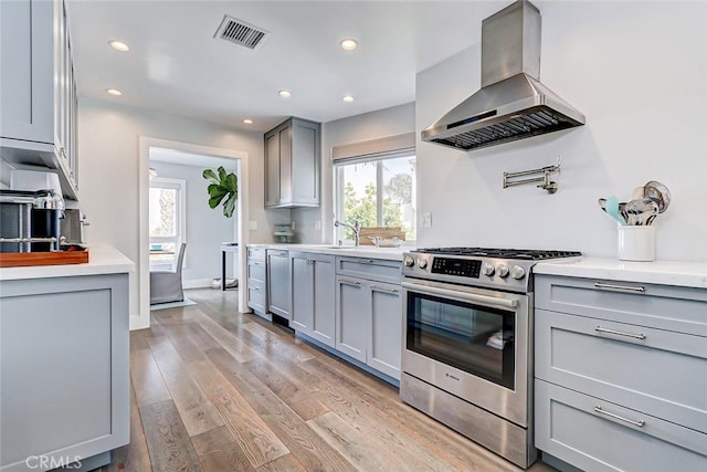 kitchen featuring gray cabinets, island range hood, sink, stainless steel gas range oven, and light hardwood / wood-style flooring