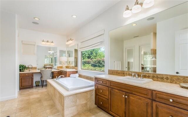 bathroom with a relaxing tiled tub, vanity, and tile patterned floors