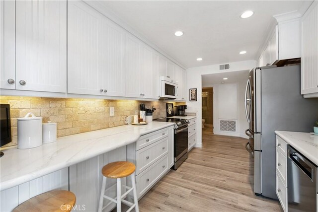 kitchen featuring light hardwood / wood-style flooring, a kitchen breakfast bar, stainless steel appliances, light stone countertops, and white cabinets