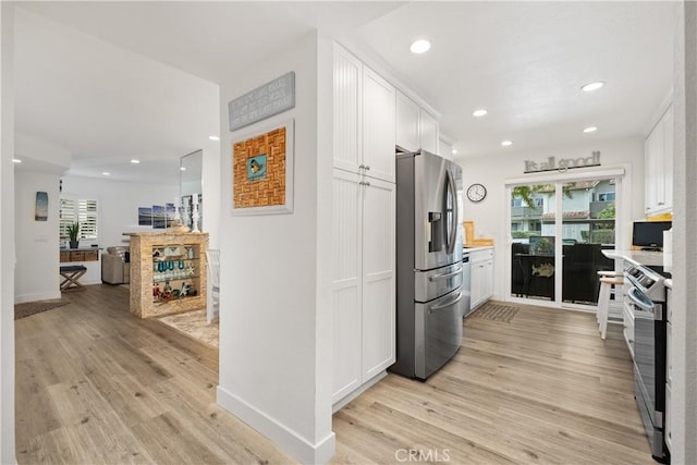 kitchen with stainless steel appliances, a healthy amount of sunlight, white cabinets, and light hardwood / wood-style flooring